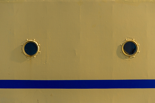 Two portholes in a yellow ship with a blue line.
