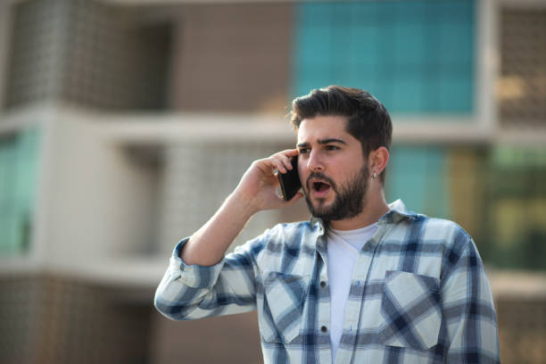 Surprised young man talking on the phone at street after work stock photo