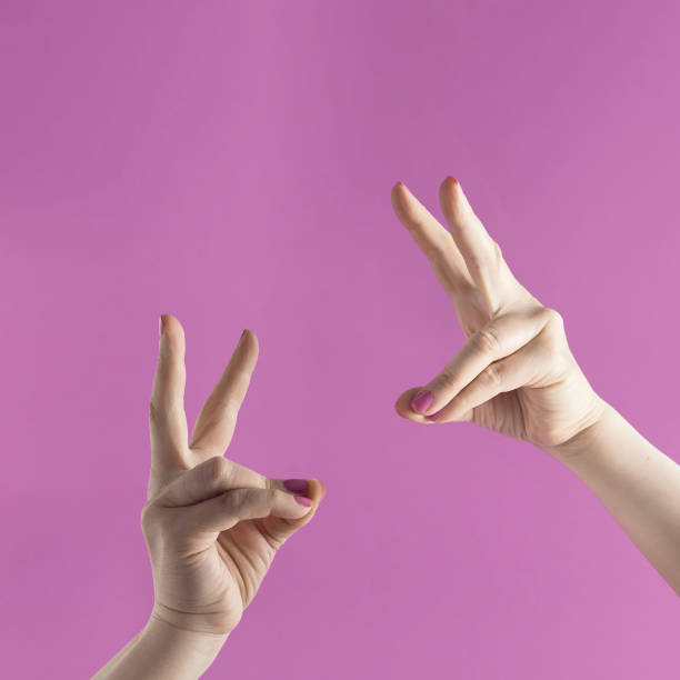 istock Modern visual with two female hands whose fingers showing bunny ears against purple background. Minimal Easter concept. Layout with copy space. 1390685107
