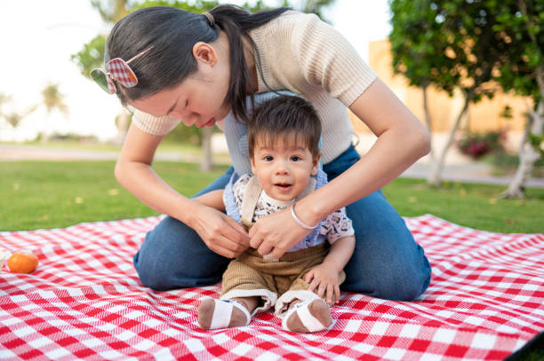 Mother wearing head protection pillow pad for her 8 months old mixed race baby boy on a picnic outdoor sitting on a picnic blanket enjoying the time outdoors
