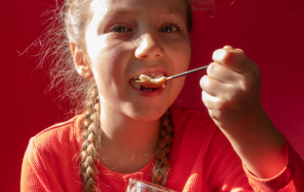 niño comiendo jalea de yogur sobre fondo rosa. dieta infantil de productos lácteos, menú de desayuno casero saludable. cuidado de la salud infantil - beauty beautiful braids dairy product fotografías e imágenes de stock