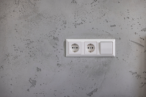 electric sockets on concrete wall with light switch.