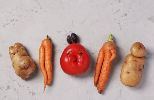 Trendy Ugly Organic Vegetables: potatoes, carrots, tomato and plum on gray background, ugly food concept, top view