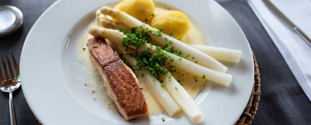 Asparagus with fried salmon White asparagus with hollandaise sauce and fried salmon on a white plate in a restaautant. Close-up. Seasonal gastronomy presented in a modern way. Top view. hollandaise sauce stock pictures, royalty-free photos & images