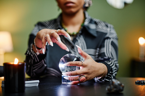 Close up of fortune teller gazing into crystal ball at spiritual seance, focus on female hands gesturing