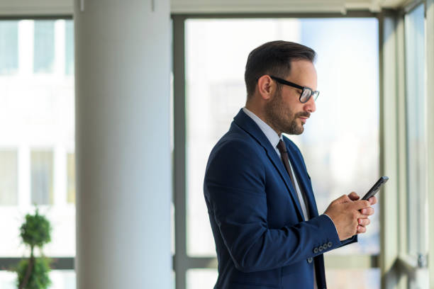 istock Young businessman standing next to window holding phone 1390702960