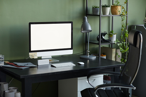 Background image of home office workplace with blank computer screen on desk against green wall, copy space