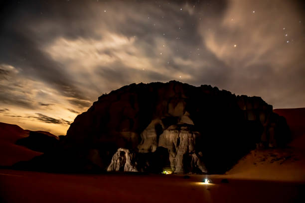 istock Camping tents enlightened under Sand dune and rocky mountain by starry sky night. 1390705598