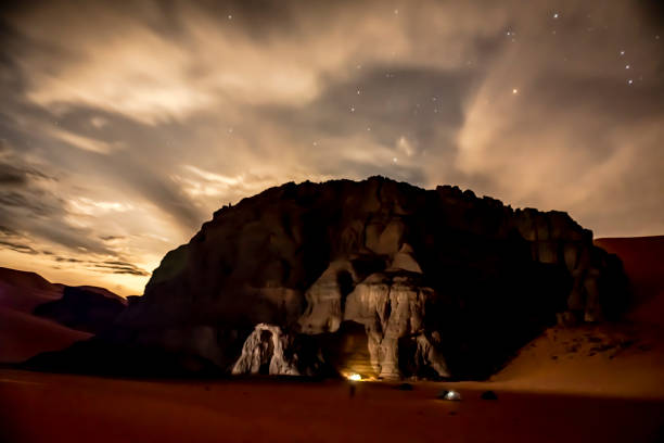 istock Camping tents enlightened under Sand dune and rocky mountain by starry sky night. 1390705720