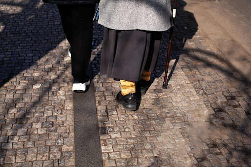 Elderly woman with a cane walking down the street, rearview. Old couple holding hands together, the concept of old age, diseases of the joints and spine.
