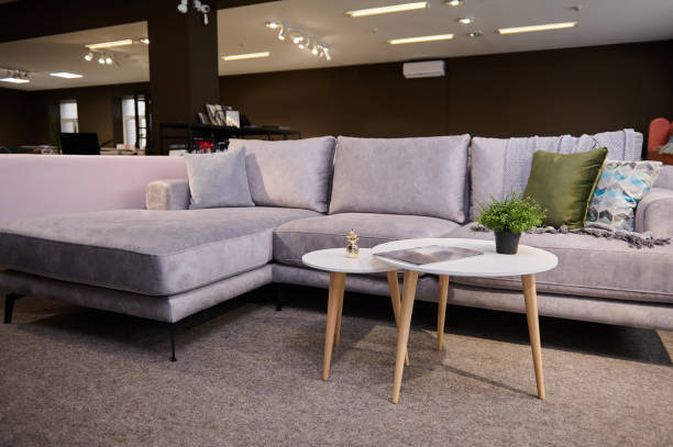 istock Comfortable upholstered settee with colored stylish cushions and small modern journal table displayed for sale in the furniture store showroom. Exhibition of upholstered furniture. 1390707711