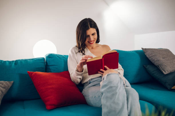 istock Woman reading a book while relaxing on a sofa at home 1390710659
