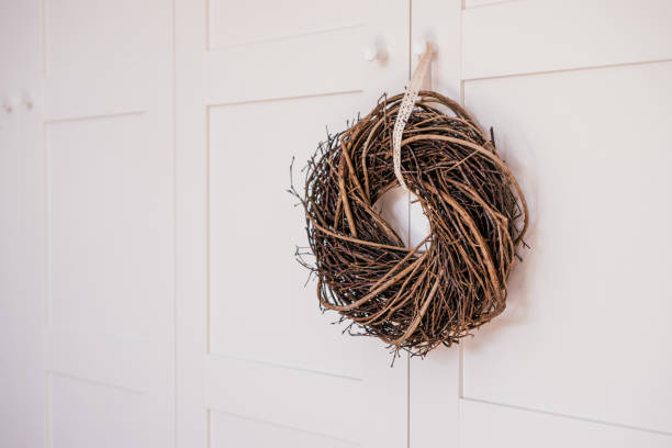 istock Woven brown hanging willow wreath from wickers with decorative white tape lace on handle wardrobe. Holiday craft symbol 1390710800