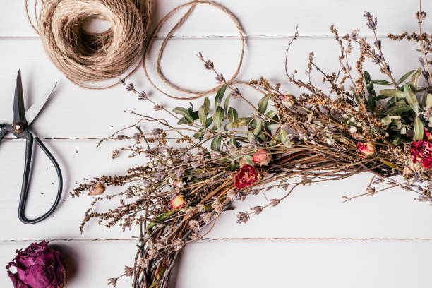 Tightly woven handmade dry herbal wreath from twigs. Skein of thread and scissors nearby on table. Florist crafting. stock photo
