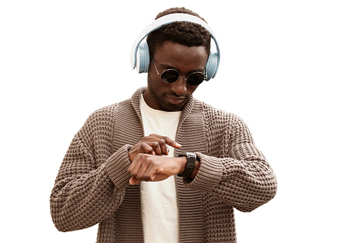 Portrait of african man in headphones looking at smart watch using voice assistant or takes calling while listening to music isolated on white background