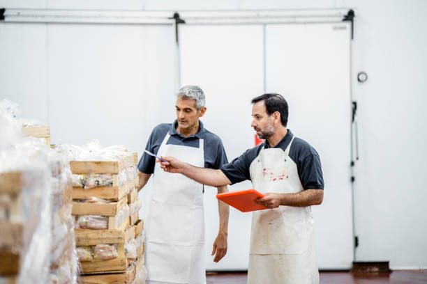 Two workers taking inventory of packaged meat wooden boxes in warehouse stock photo