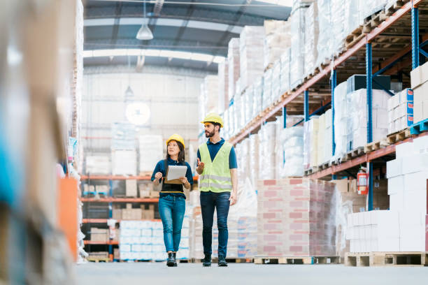 Two employees checking inventory on warehouse racks Male and female workers discussing over stock checklist in warehouse. Multi-ethnic colleagues are working together at distribution warehouse, walking by the racks and looking the stock levels. freight transportation stock pictures, royalty-free photos & images