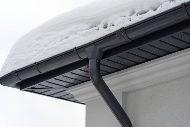 Metal Downpipe system, Guttering System, External downpipes and drainage pipes under snow. Corner of house with roof made of gray metal tiles and gutter covered with thick layer of snow in winter. stock photo