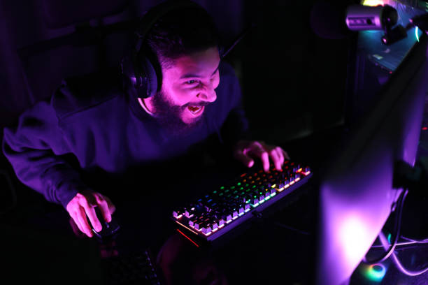 istock A young man plays a computer game in a room lit up with colorful neon lights. Playing the game is fun and satisfying. in the black studio A man wearing headphones intends to play a game on the Internet. 1390722743