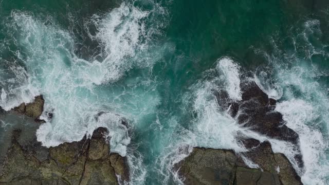 Waves crash against rocks in the ocean. A peaceful picture of nature. Aerial view of the rocks in water. The meeting place of the ocean and land. 120 fps video