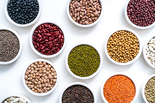 Dried legumes assorted in many bowls on white background including lentils, chickpeas, soybeans and beans