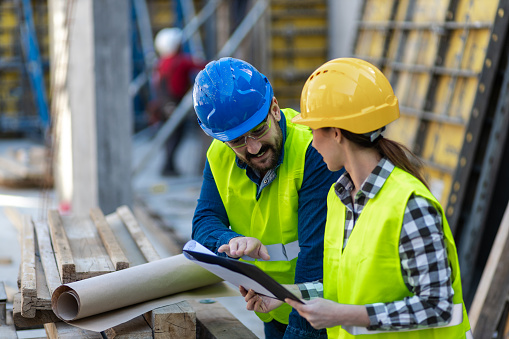 Attractive young construction engineers brainstorming on construction site. Looking at blueprints.