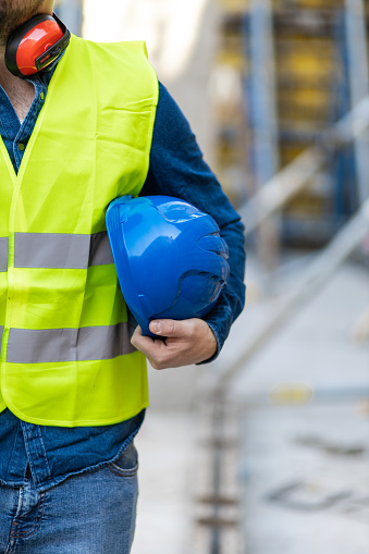 Construction worker holding blue helmet close up. Working at construction site.