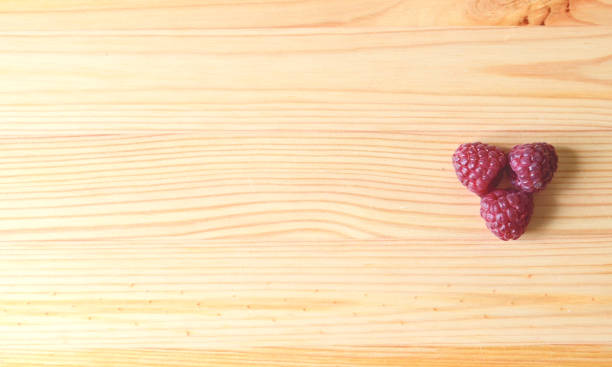 Three red raspberries on a wooden table stock photo