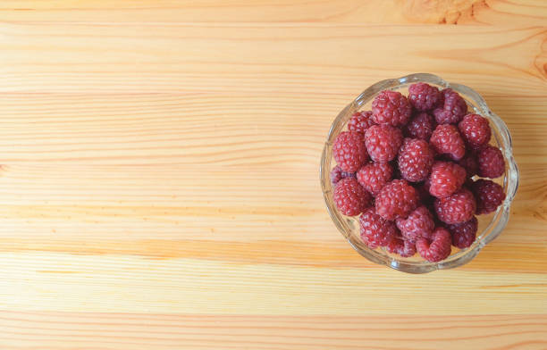 Red raspberries in a glass bowl on a wooden table stock photo