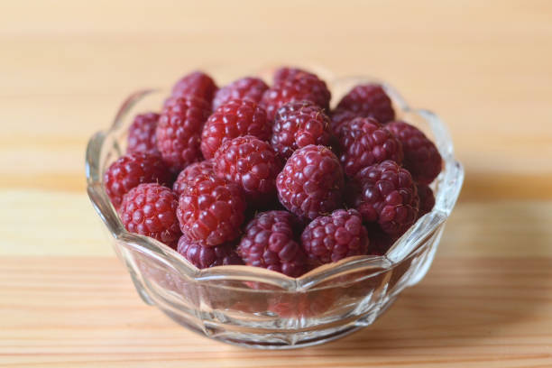 Red raspberries in a glass bowl on a wooden table stock photo