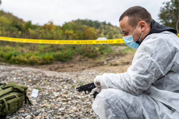 side view of the police detective forensic investigator on the crime scene hold gun evidence on the beach or sand rocks used for murder or shooting with tag during investigation copy space - gun men spy suit imagens e fotografias de stock