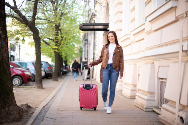 istock Young woman walking and pulling a small wheeled luggage 1390734220