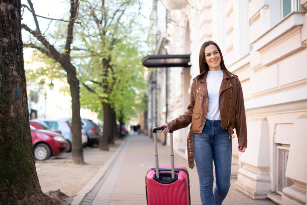 istock Young woman walking and pulling a small wheeled luggage 1390734226