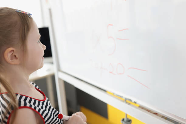 istock Toddler writing solution of sums on white board at school, educational process 1390738776