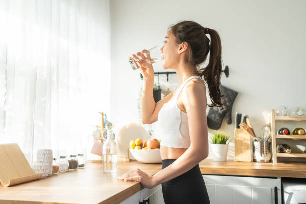 asian beautiful woman in sportswear drink water after exercise at home. young thirsty active sport girl takes a sips of clean mineral natural in cup after workout for health care in kitchen in house. - dranken stockfoto's en -beelden