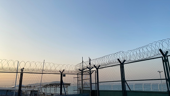 Storm clouds pass over the razor wire, barbed wire and wire mesh fences surrounding Sydney Kingsford-Smith Airport.   This image was taken from near Shep's Mound, a public viewing area off Ross Smith Avenue, at sunset on 10 February 2023.