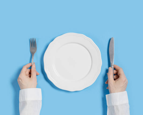 istock White plate with metal cutlery set on blue background. Empty ceramic dinner plate, woman hands hold knife and fork, top view, mock up, copy space. View from above, flat lay style 1390762399