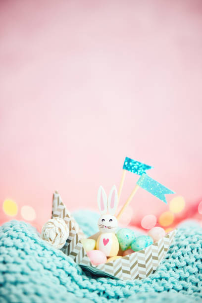 Easter background with origami boat filled with candy Easter eggs and a cute wooden Easter bunny