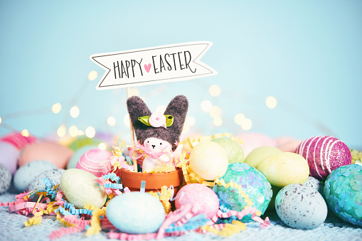 Easter bunny in a plant pot surrounded by lots of vibrant colored Easter eggs and a HAPPY EASTER sign