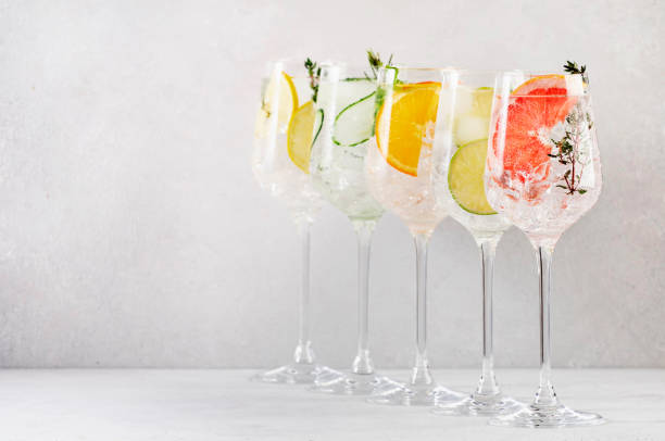 istock Gin and tonic cocktails set. Trendy Alcoholic drinks with lime, lemon, grapefruit, orange, cucumber, soda and spicy herbs in wine glasses, gray background. Summer cocktail party 1390765365