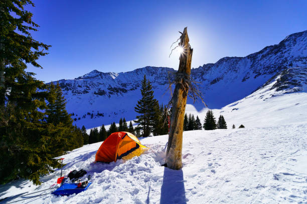 High Mountain Ski Camping High Mountain Ski Camping - Ski mountaineering at high altitude with colorful orange tent perched on mountain ridge with skis and rugged mountains in background. tenmile range stock pictures, royalty-free photos & images