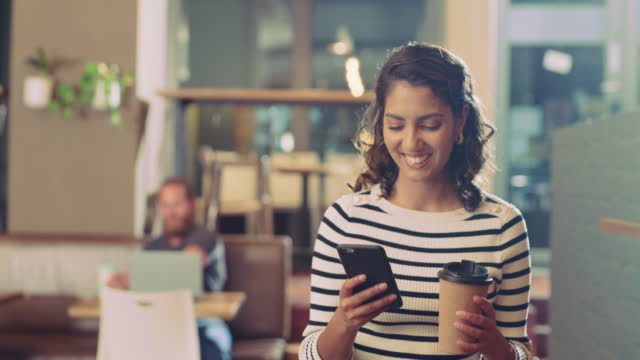 4k video footage of a young woman using a smartphone and having coffee in a cafe