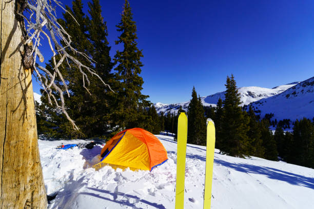 High Mountain Ski Camping High Mountain Ski Camping - Ski mountaineering at high altitude with colorful orange tent perched on mountain ridge with skis and rugged mountains in background. tenmile range stock pictures, royalty-free photos & images