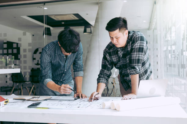 istock Architects or engineering working with blueprints and discussing project together at the meeting in the office. 1390769129