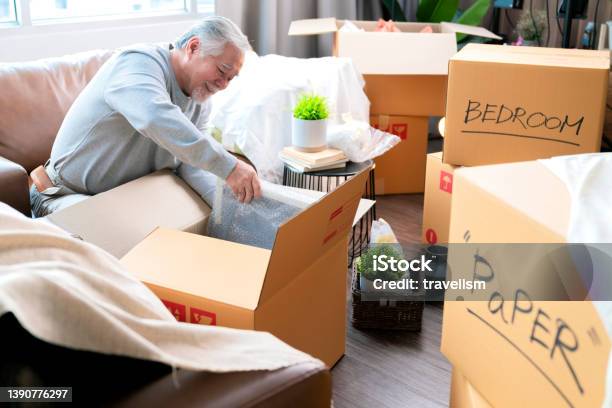Horizontal Medium Shot Of Adult Elder Senior Asian Man Male White Beard Sitting On Floor Preparing For Moving To New House Packing Things Into Boxes And Taping Them In Living Roomhome Moving Ideas Concept Stock Photo - Download Image Now