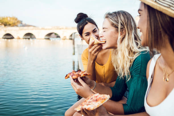 Diverse young women friends eating italian take away pizza in city street Diverse young women friends eating italian take away pizza in city street - Multiracial female having fun together on summer vacation - Copy space for text italian ethnicity stock pictures, royalty-free photos & images