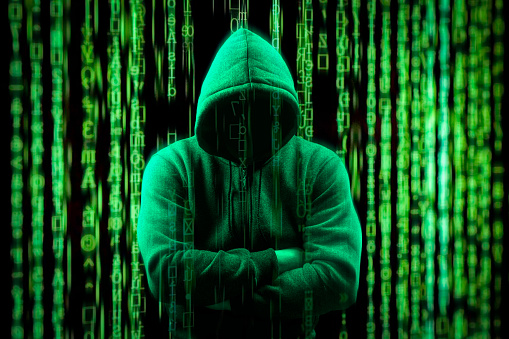 hacker Silhouette on dark green binary background. Hacker on matrix digital background. Hacking and malware concept. Be aware of hacker attack. Faceless hooded anonymous computer hacker