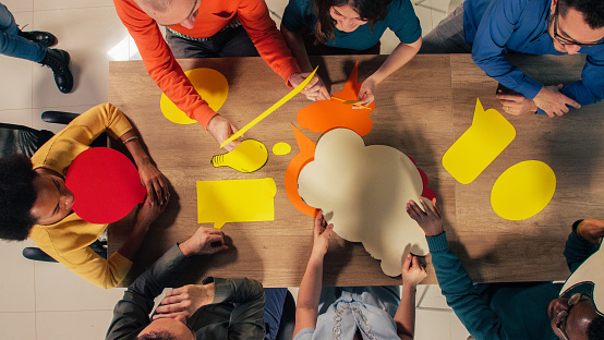 Directly above shot of team of diverse entrepreneurs sitting around conference table, assembling colorful, blank thought bubbles when brainstorming new ideas.