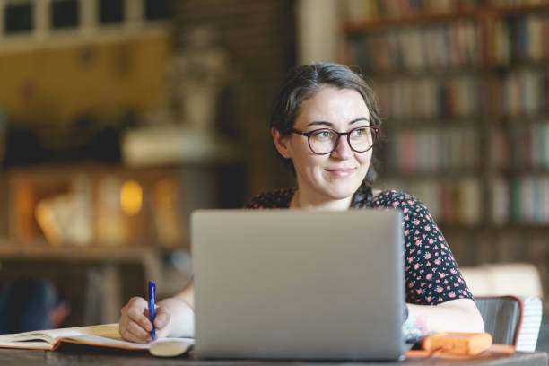 istock Woman at the library with laptop, taking notes to a notebook 1390787773