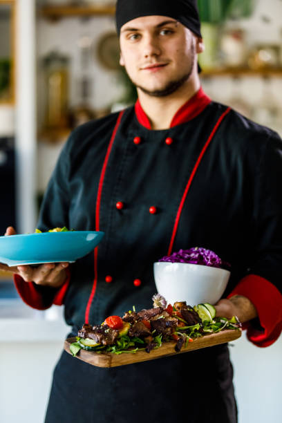 istock Young chef holding dishes he prepared and smiling at camera 1390787830
